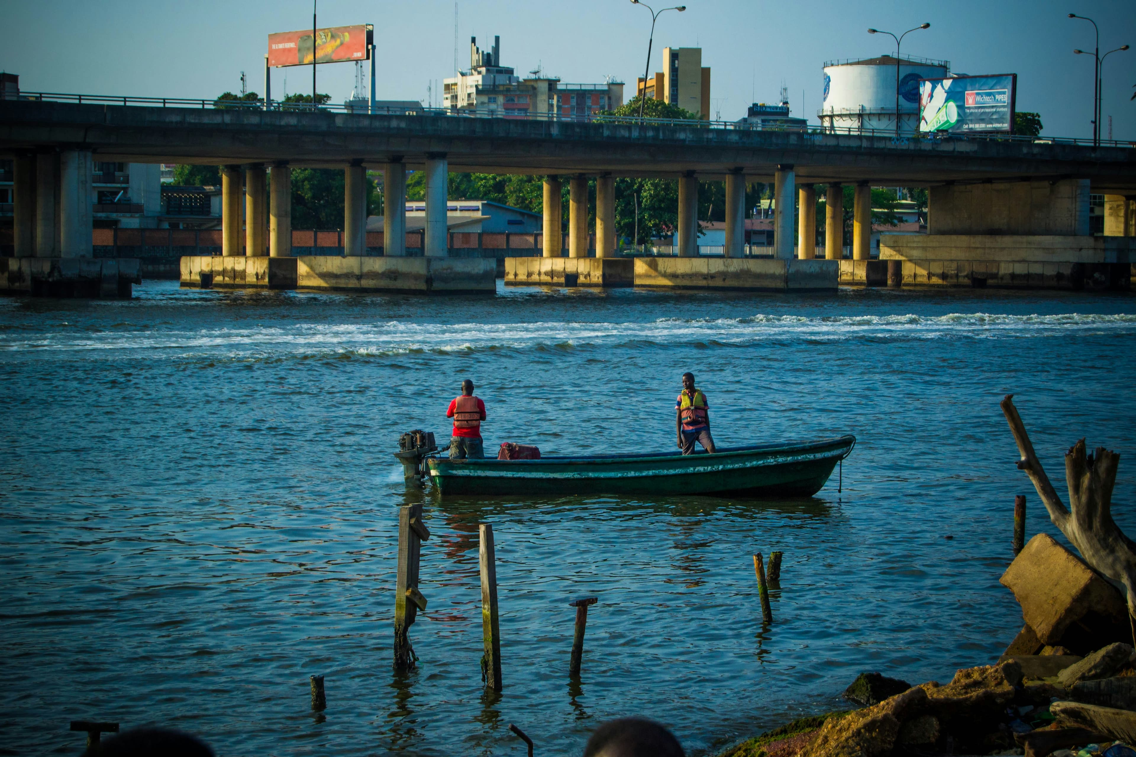 Two boatmen crossing the lagoon beneath an expressway bridge.