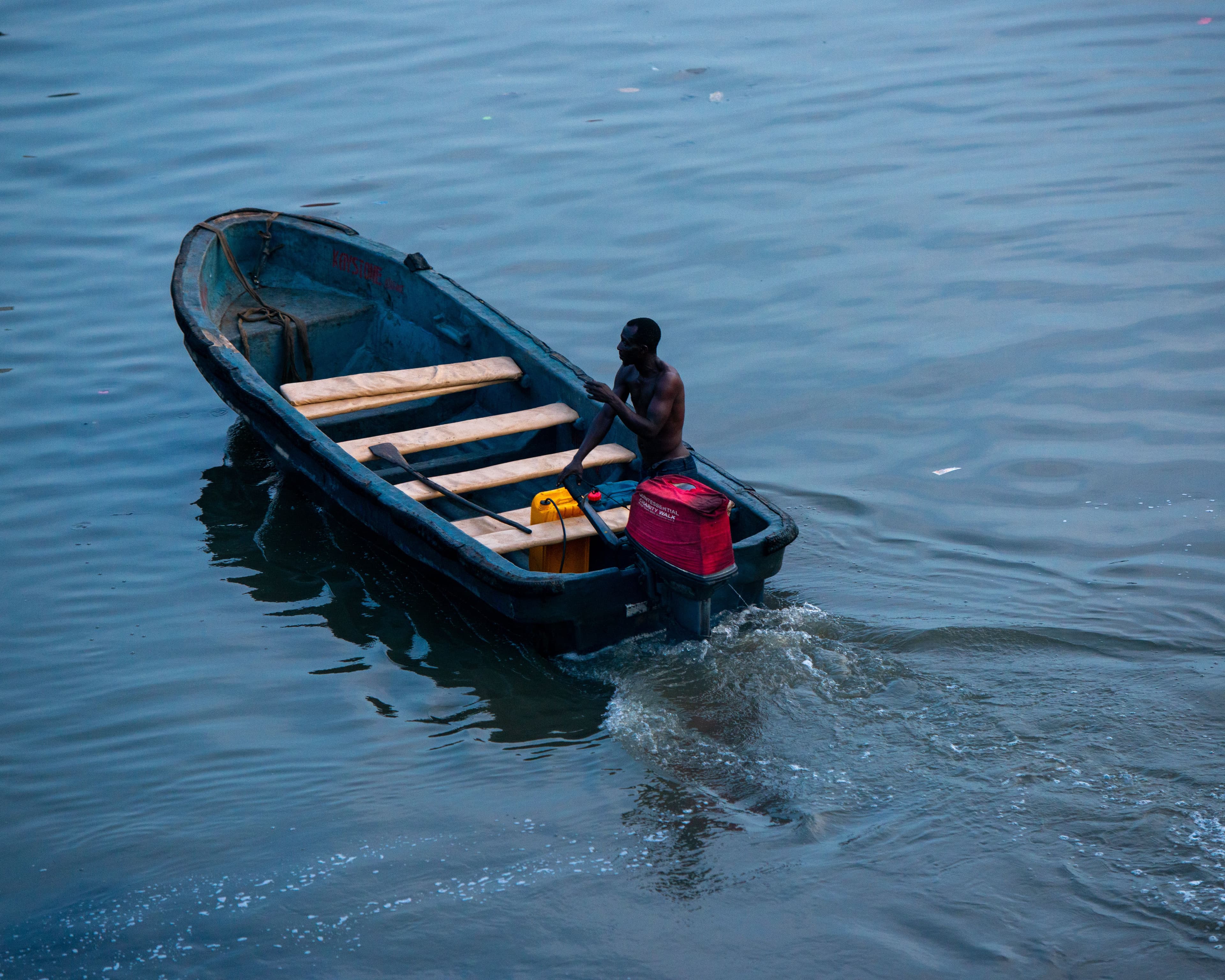 A boatman steering across the calm lagoon at dusk.