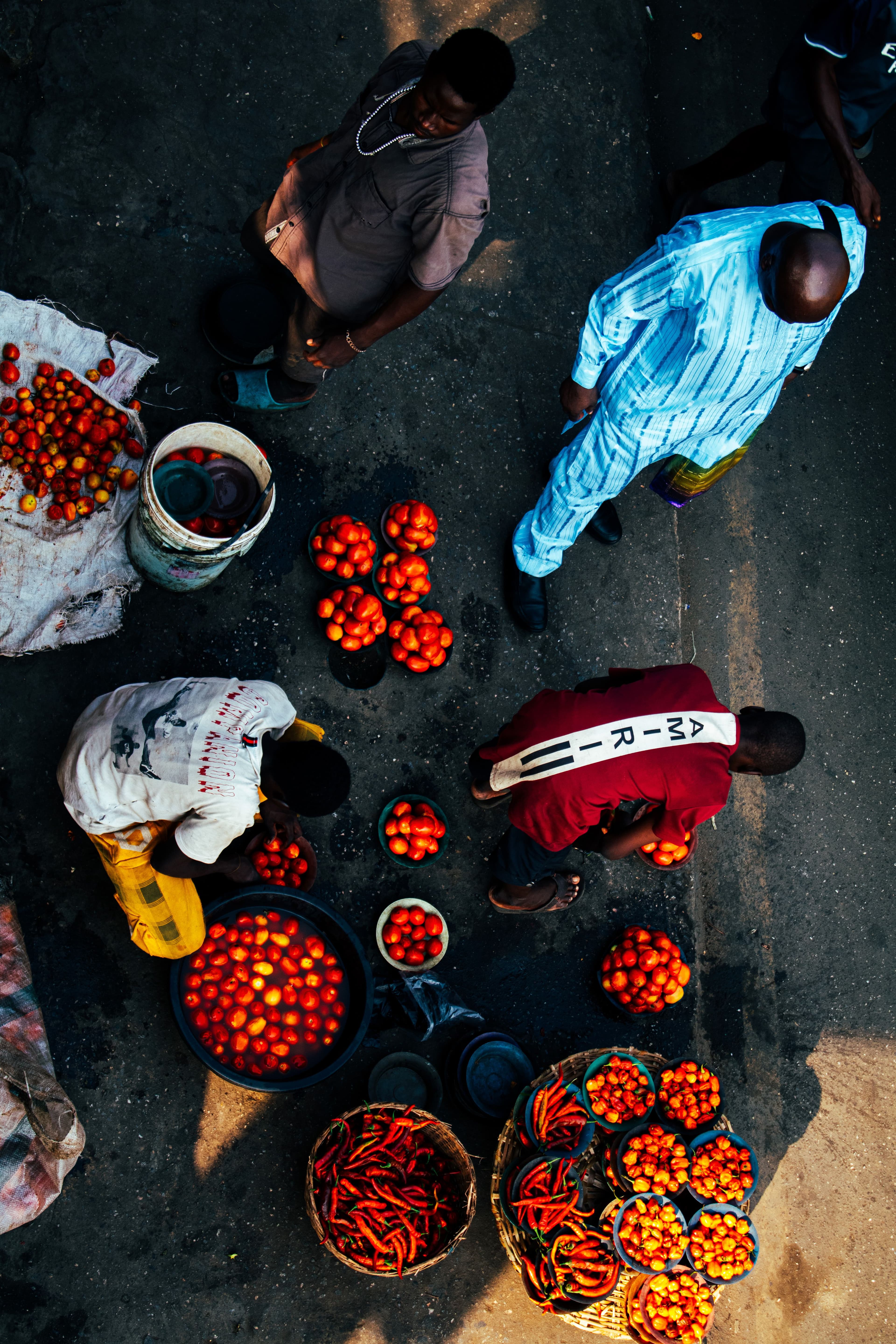 Tomatoes and peppers laid out for sale on a market street, seen from above.