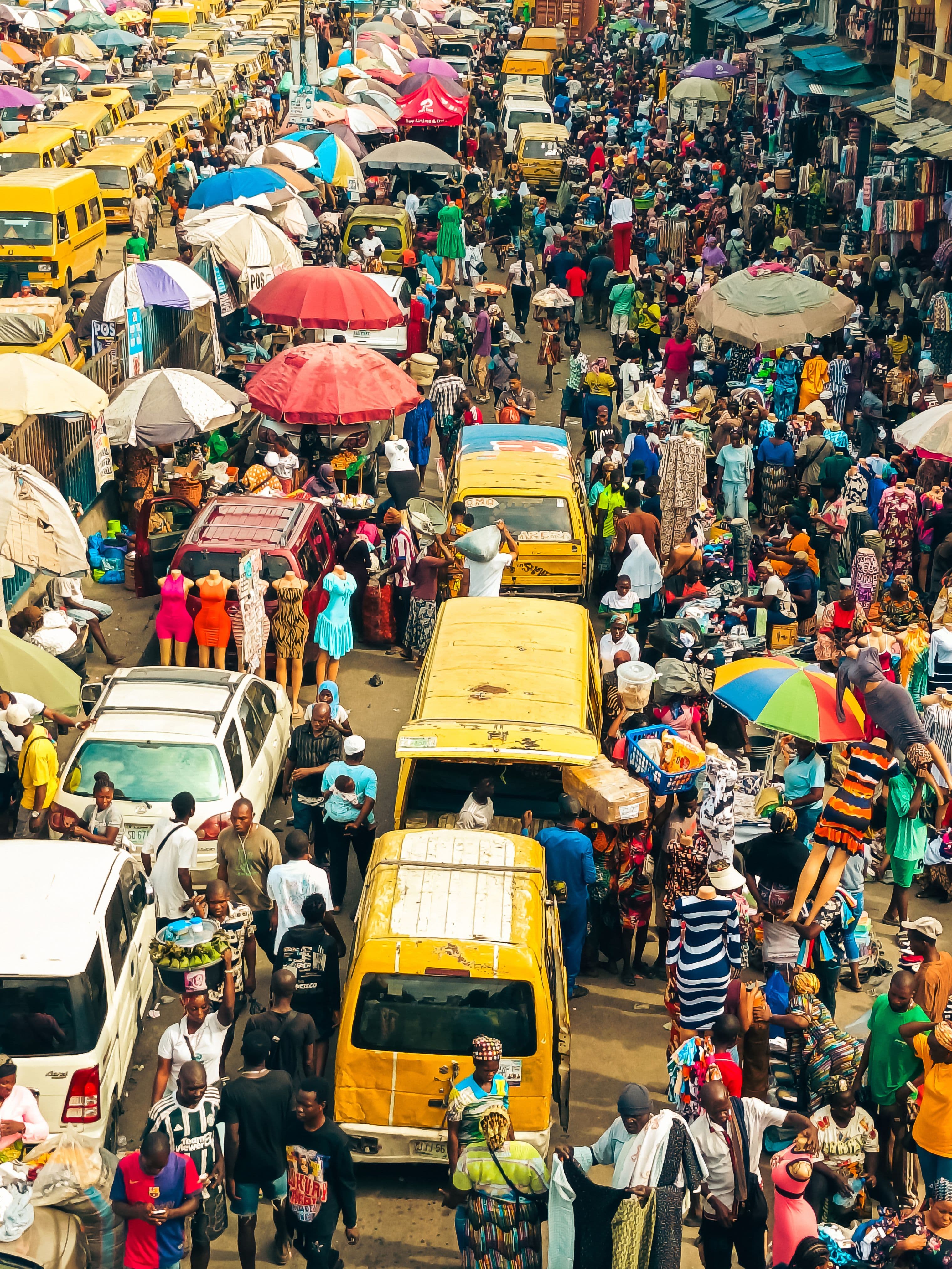 A crowded market street on the Lagos mainland, packed with stalls, buses, and shoppers.