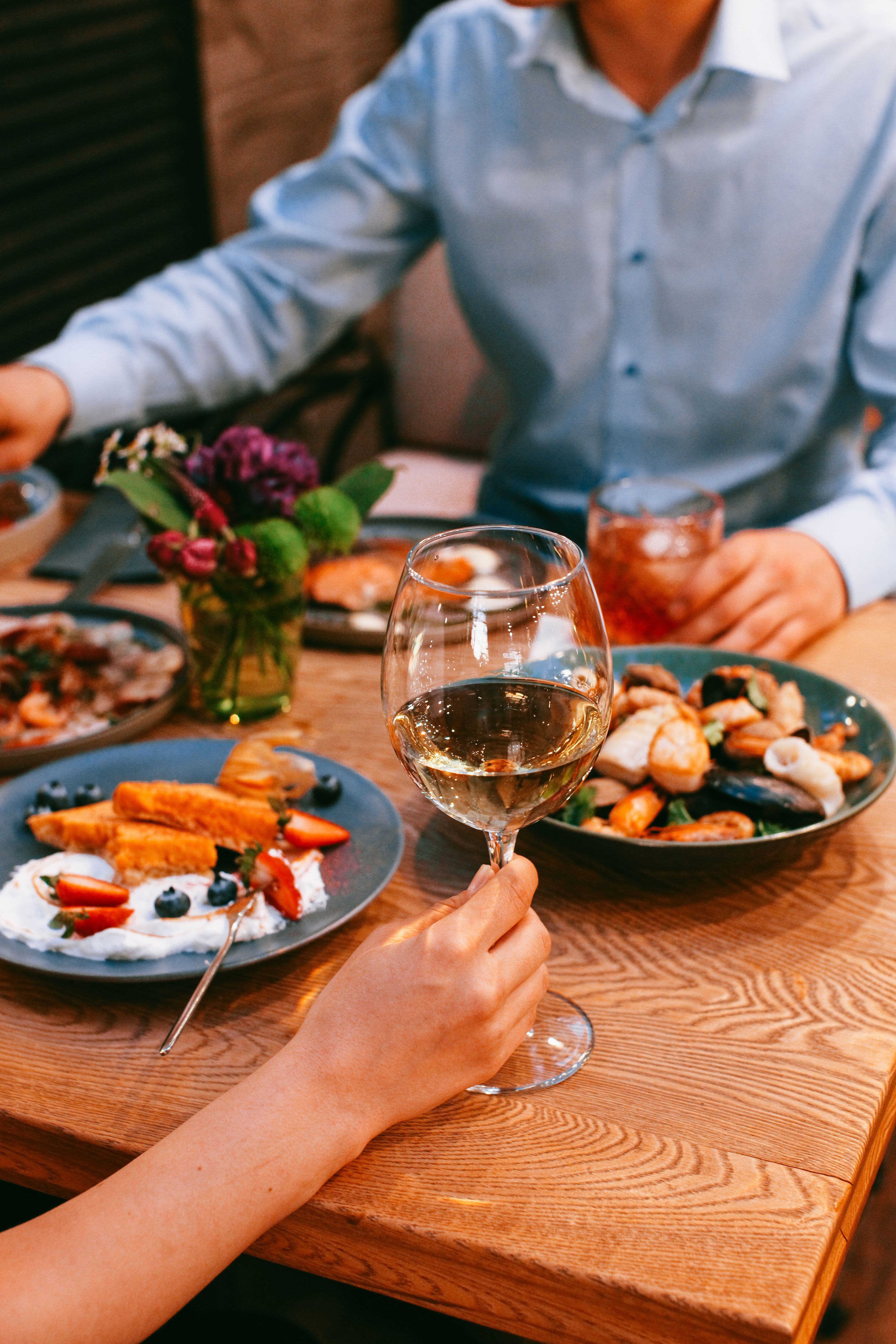 Shared plates and a glass of wine at a long wooden dinner table.